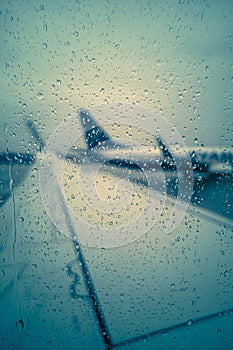 The concept of flight delay or cancellation, raindrops on the glass against the background of a wing and a standing plane