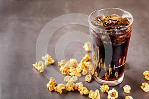 The concept of food for the cinema, for watching a movie. Cold cola drink with ice in a glass filled with popcorn