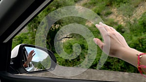 Concept of freedom, autotravel and adventure. A woman driver feels the wind through her hands while driving along a road