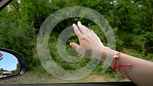 Concept of freedom, autotravel and adventure. A woman driver feels the wind through her hands while driving along a road