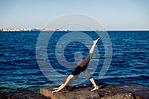 Concept freedom of female energy. Young woman practices yoga on background of sea, wind blows hair