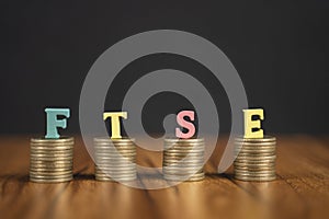 Concept of FTSE or Financial Times Stock Exchange showing with coins and letters on black background.