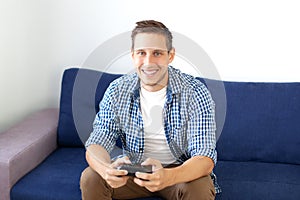 The concept of the game. the guy is playing a video game with a joystick at home. A smiling man in a shirt, sitting on the couch,