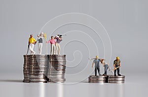 Concept of the gap between rich and poor. Miniature people standing on a pile of coins.