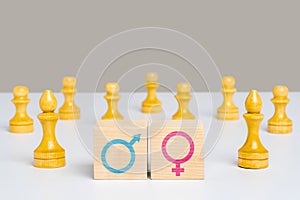 The concept of gender equality and equal pay for work. Wooden cubes with symbols of men and women among chess pieces pawns and