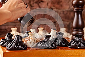 Concept of Georgian cuisine. black and white khinkali stand on a chessboard. female hand takes khinkali. khinkali with barinas,