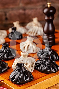 Concept of Georgian cuisine. black and white khinkali stand on a chessboard. female hand takes khinkali. khinkali with barinas,