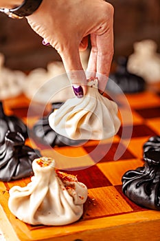 Concept of Georgian cuisine. black and white khinkali stand on a chessboard. female hand takes khinkali. khinkali with barinas,