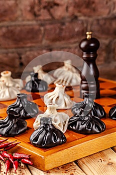 Concept of Georgian cuisine. black and white khinkali stand on a chessboard. female hand takes khinkali. khinkali with barinas,