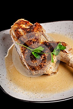 The concept of Georgian cuisine. Half a baked chicken in garlic sauce with crispy crust on a white plate, on a black background