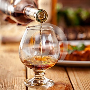 Concept of Georgian restaurant. A girl pours Georgian brandy from bottle into glass. On wooden table is hachipuri