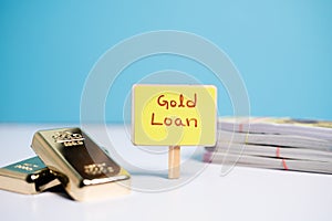 Concept of gold loan showing wiyh Gold loan sign board with Gold bars and currency notes on table