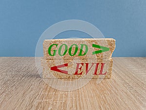 Concept green word Good and Evil on brick blocks. Beautiful wooden table, blue background. Sign Shows Difference Between Moral