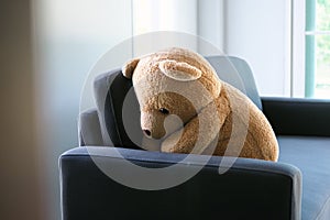 The concept of grief of children. The teddy bear sits on the couch inside the house, alone looking sad and disappointed