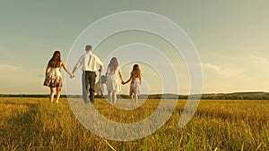 Concept of a happy childhood. mother, father and little daughter with sisters walking in field in the sun. Happy young