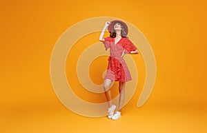 Concept happy emotional young woman in red summer dress and hat jumping   on yellow background