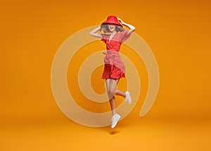 Concept happy emotional young woman in red summer dress and hat jumping   on yellow background