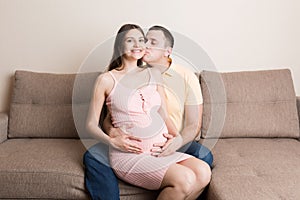 Concept happy family in anticipation of the birth of a baby. Pregnant woman and her husband cuddling on the sofa at home