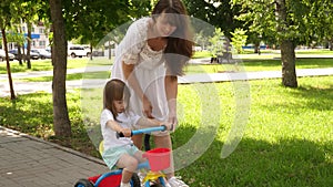 Concept of happy family and childhood. child learns to ride bicycle. parents and little daughter walks in park. Happy