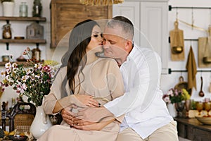 Concept-a happy man hugs his pregnant wife`s stomach while sitting in the kitchen