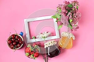 The concept of harvesting in the summer.Jars of jam, strawberries in a cup, cherries in a blue cup, a bouquet of flowers on a pink