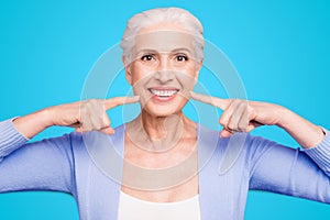 Concept of having strong healthy white perfect teeth at old age. Portrait of old lady with beaming smile pointing on her