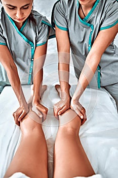 Concept of healthcare and female beauty. Two masseuses make a double legs and feet massage of a girl in a spa salon