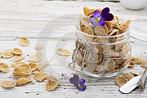 The concept of a healthy breakfast of whole wheat cereals, berries and edible flowers on a garden violet on a light