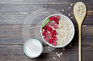The concept of healthy diet. Breakfast with oatmeal and raspberry. Wooden, spoon, milk in a glass, mint. Wooden dark background.