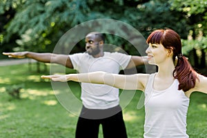 Concept of healthy family lifestyle and yoga at park. Young multiethnic couple exercising outdoors with arms