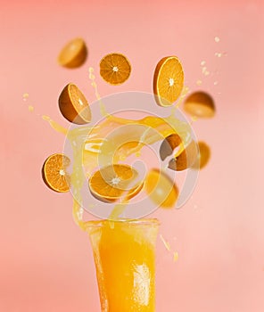 Concept of healthy food, fresh juice, splashes drops from orange slices fly out of bottle, on a pink background