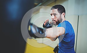 Concept of a healthy lifestyle.Bearded muscular man fighter practicing kicks with punching black bag.Kick boxer boxing