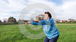 Concept of a healthy lifestyle and sports. Smiling elderly woman in sportswear performs a squat exercise in the park