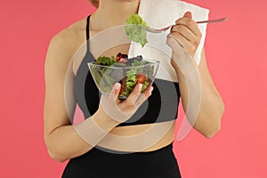 Concept of healthy lifestyle, woman eats salad on pink background