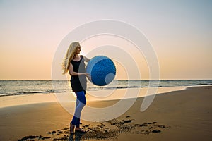 Concept of healthy lifestyle for women. Smiling young female with long blonde hair with big blue ball