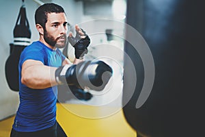 Concept of a healthy lifestyle.Young muscular man fighter practicing kicks with punching bag.Kick boxer boxing as