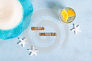 Concept hello summer text, hat, cocktail with orange and starfish on blue background top view