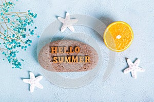 Concept hello summer text on stone, orange, starfish and seashells on blue background top view