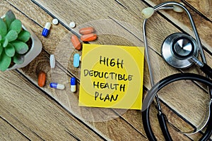 Concept of High Deductible Health Plan write on sticky notes with stethoscope isolated on Wooden Table