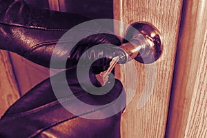 Concept home protection. Thief in black gloves opens a wooden door with key. Close-up