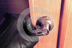 Concept home protection. Thief in black gloves opens a wooden door with wire