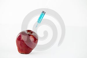 Concept: human GMO manipulation of nature and relative poisoned fruits. Close-up of an apple contaminated with a syringe threaded