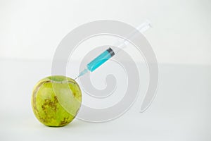 Concept: human GMO manipulation of nature and relative poisoned fruits. Close-up of an apple contaminated with a syringe threaded