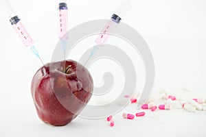 Concept: human GMO manipulation of nature and relative poisoned fruits. Close-up of an apple contaminated with a syringe threaded