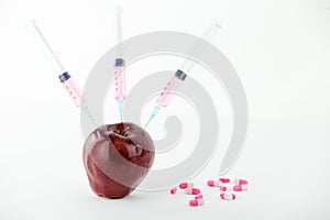 Concept: human GMO manipulation of nature and relative poisoned fruits. Close-up of an apple contaminated with a syringe threaded