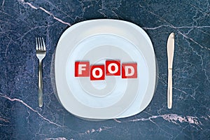 The concept of hunger and food scarcity. An empty white plate with the word FOOD on red wooden cubes