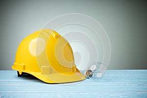 Concept idea design, and safety on work. Personal protective equipment. Yellow hard hat with lighting bulb on blue wooden table