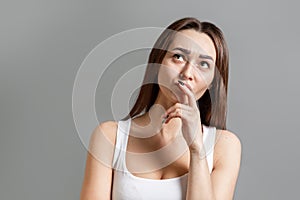 Concept of idea and information search. Portrait of a pensive young Caucasian woman who looks up with a frown. Gray background.
