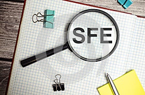 Concept image of Accounting Business Acronym SFE Sales Force Effectiveness written on white notebook with magnifying glass