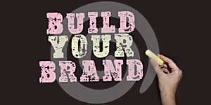 Concept image Build Your Brand written over blackboard with pink and yellow chalk, Branding marketing startup concept